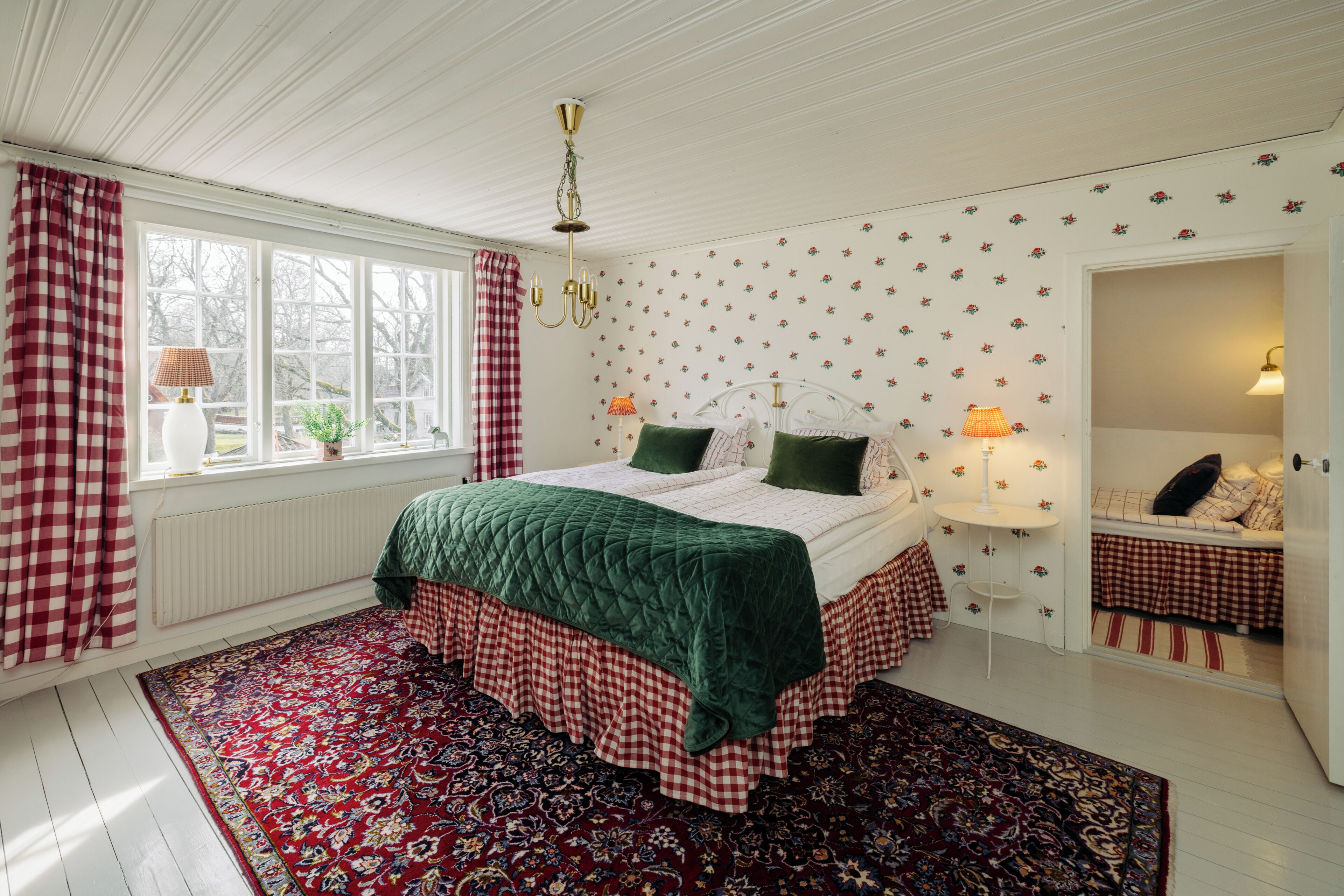 A bedroom with a bed, a window, a radiator, a wall-mounted lamp, and a mirror.