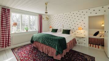 A bedroom with a bed, a window, a radiator, a wall-mounted lamp, and a mirror.