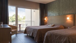 Habitación de hotel con dos camas, un escritorio y un balcón con mesa y sillas.