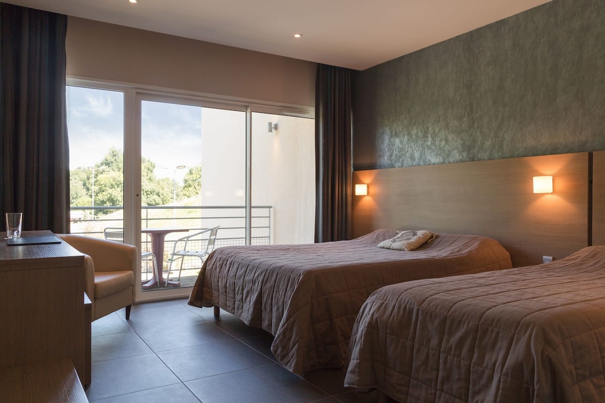 Habitación de hotel con dos camas, un escritorio y un balcón con mesa y sillas.