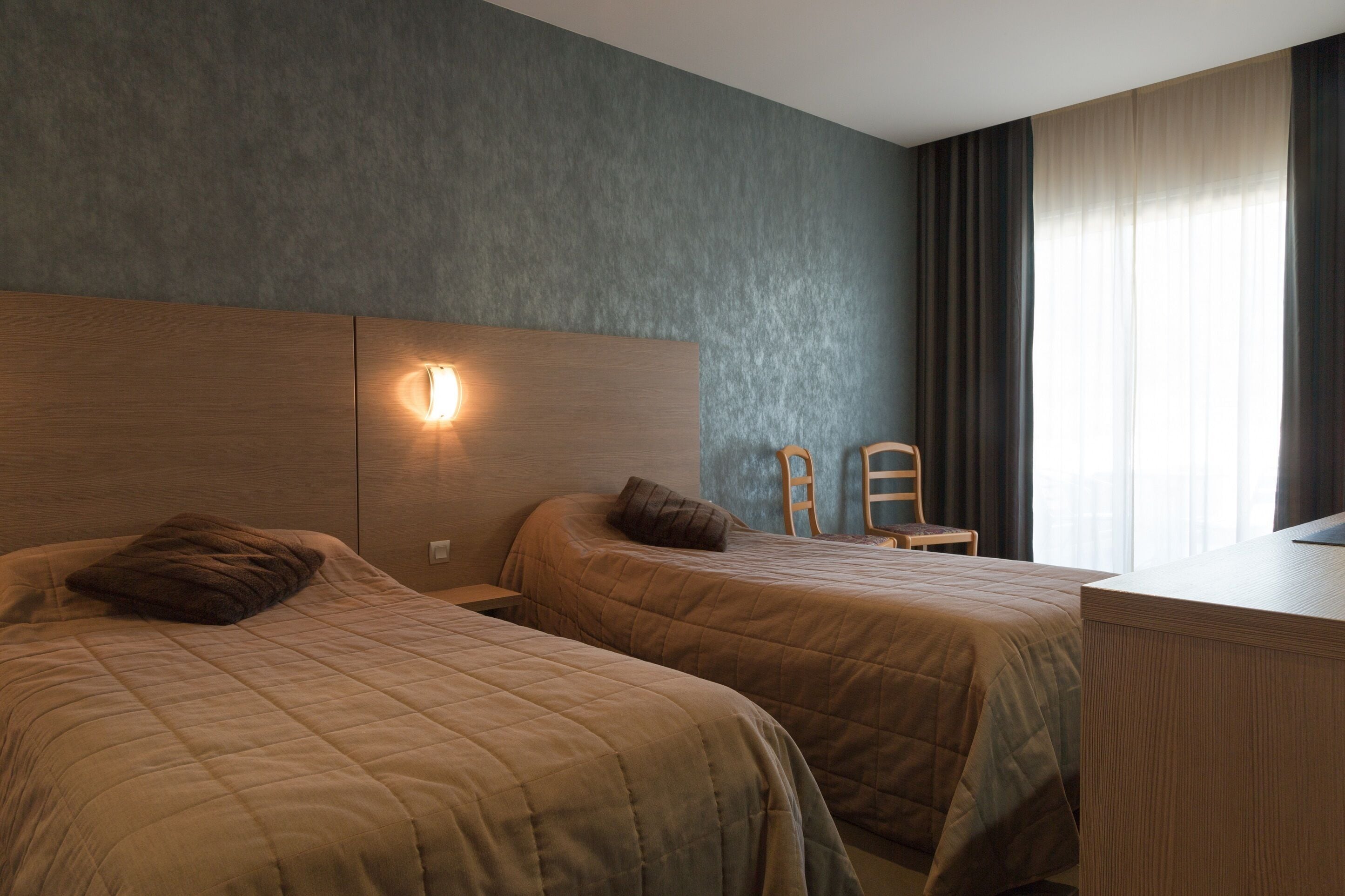A hotel room with two beds, a desk, and a window with curtains.