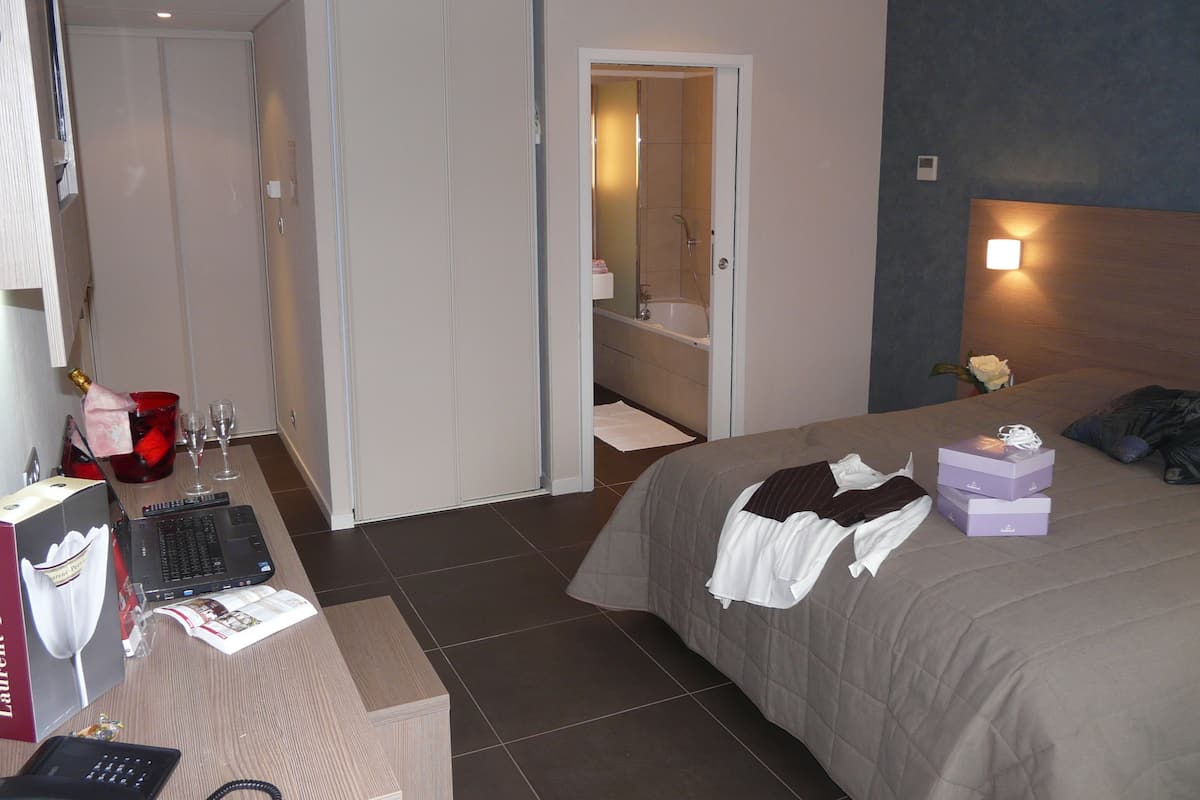 Habitación de hotel con cama, escritorio con una computadora portátil, una botella de champán y zona de ducha.