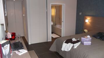 A hotel room with a bed, a desk with a laptop, a bottle of champagne, and a shower area.