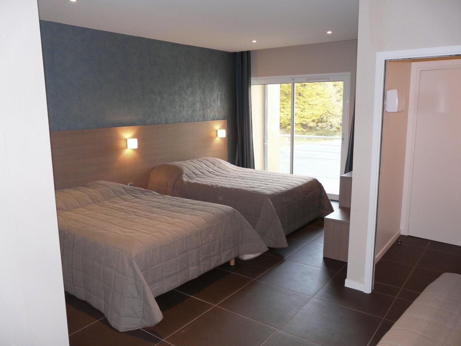 Une chambre d’hôtel moderne avec deux lits, une grande fenêtre et une vue sur l’extérieur.