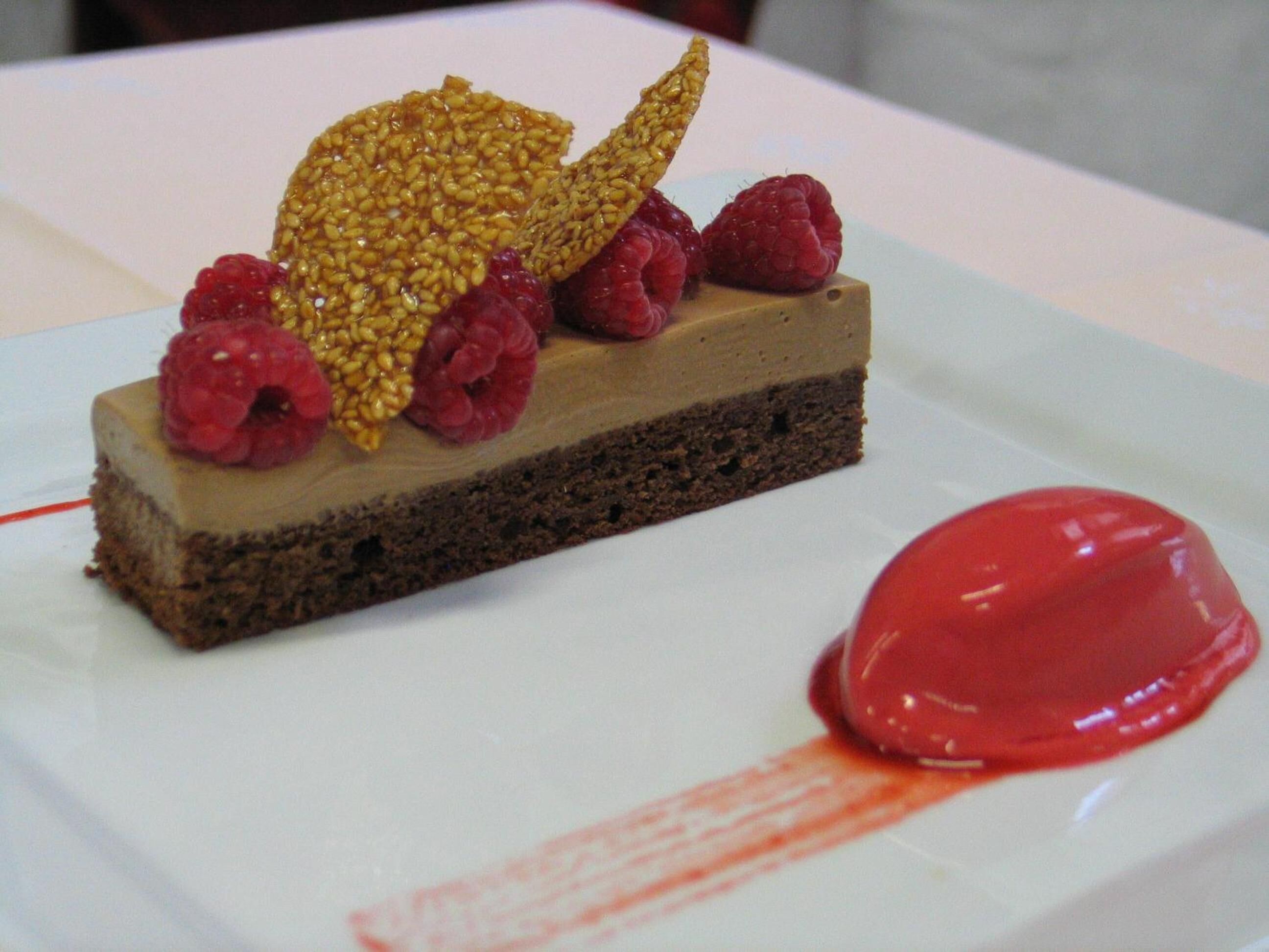 Un dessert aux framboises et aux graines de sésame, présenté sur une assiette blanche.