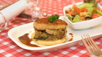 A plate with a meat sandwich and a side salad on a red and white checkered tablecloth.