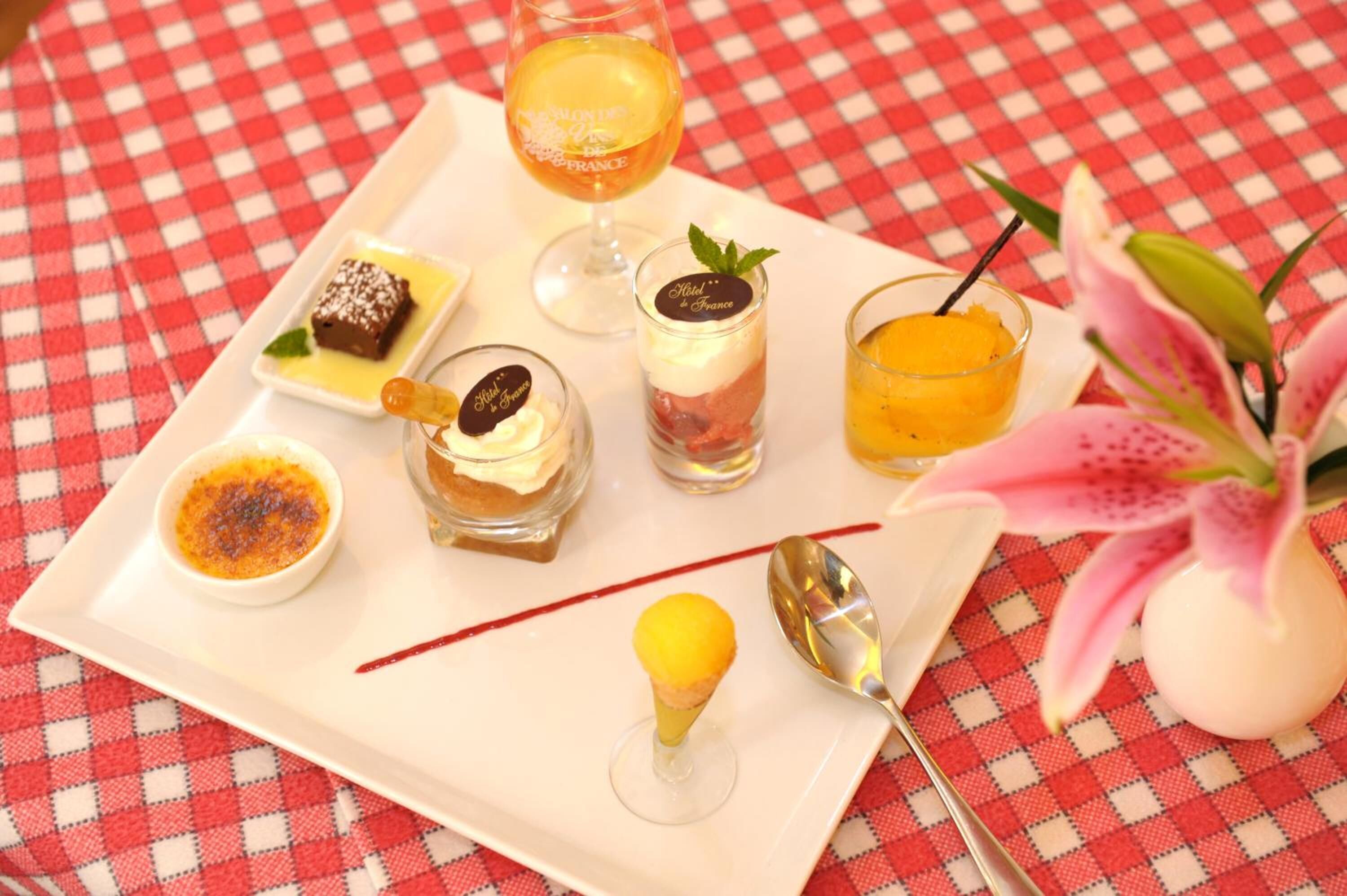 A tray with various desserts and a glass of orange juice on a checkered tablecloth.