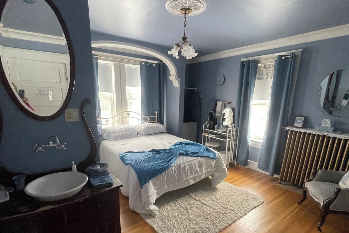 A bedroom with a bed, a dresser, a mirror, a radiator, and a chair.