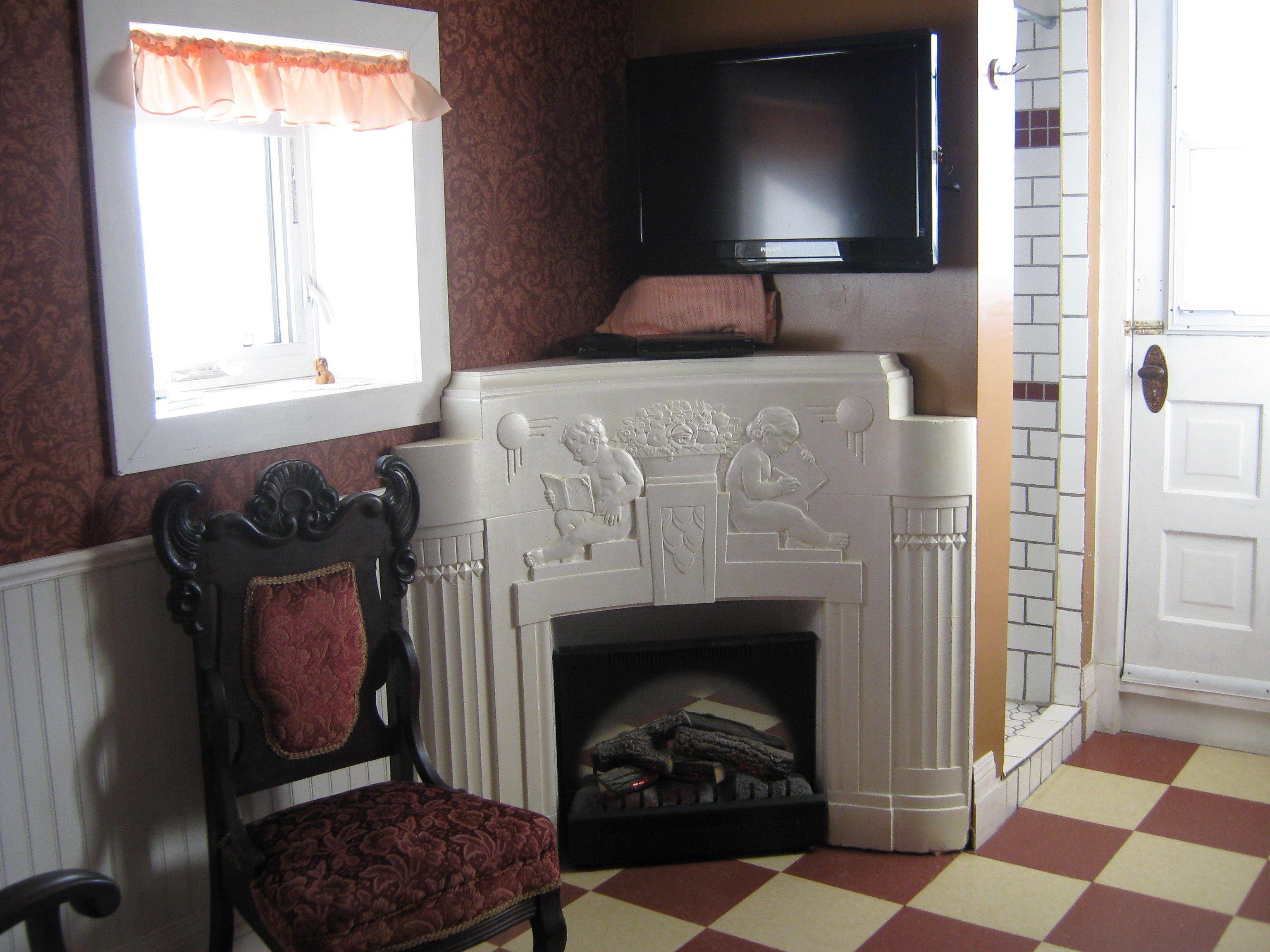 A room with a fireplace, a television mounted above it, a chair with a red cushion, and a checkered floor.