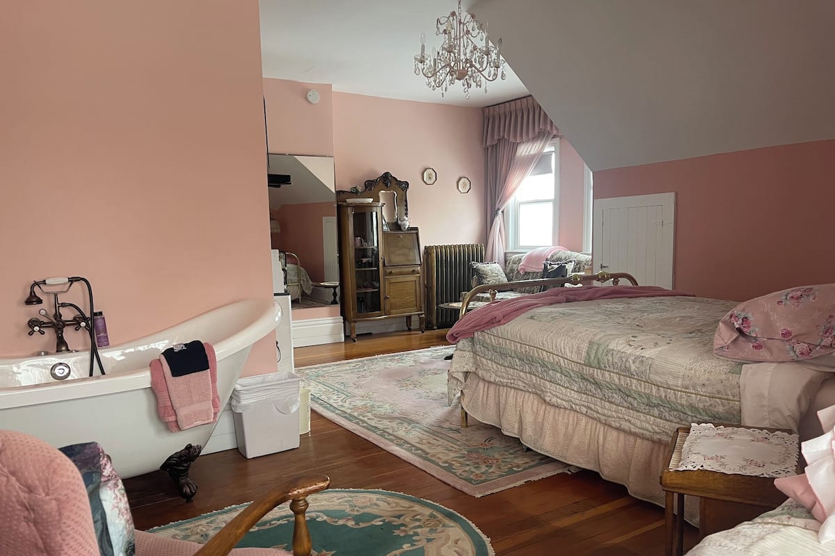 A bedroom with a bed, a dresser, a mirror, a radiator, and a chandelier.