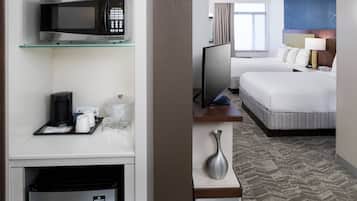 A hotel room with a microwave, coffee maker, and a minibar. There are two beds with white bedding and a TV on a stand.
