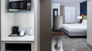 A hotel room with a microwave, coffee maker, and a TV on a stand.