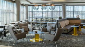 A modern hotel lobby with a seating area, large windows, and a central table.