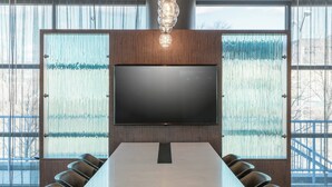 A conference room with a large flat-screen TV, a long table, and six chairs.