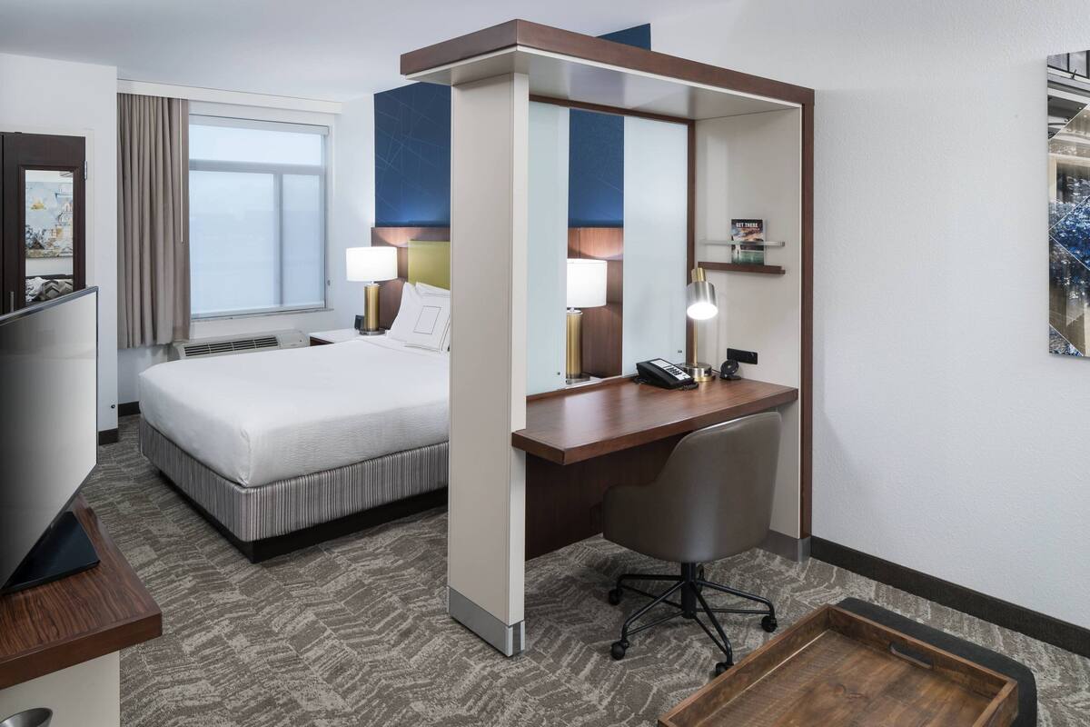 Een hotelkamer met een bed, bureau, stoel en een groot raam.