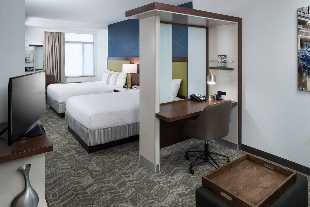 Een hotelkamer met twee bedden, een bureau, een stoel, een televisie en een klein tafeltje.