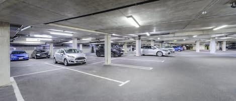 Un parcheggio sotterraneo su più livelli con pilastri in cemento e illuminazione al neon.