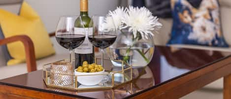 Une table en bois sur laquelle se trouvent une bouteille de vin, deux verres à vin, un bol d’olives et un vase rempli de fleurs blanches.