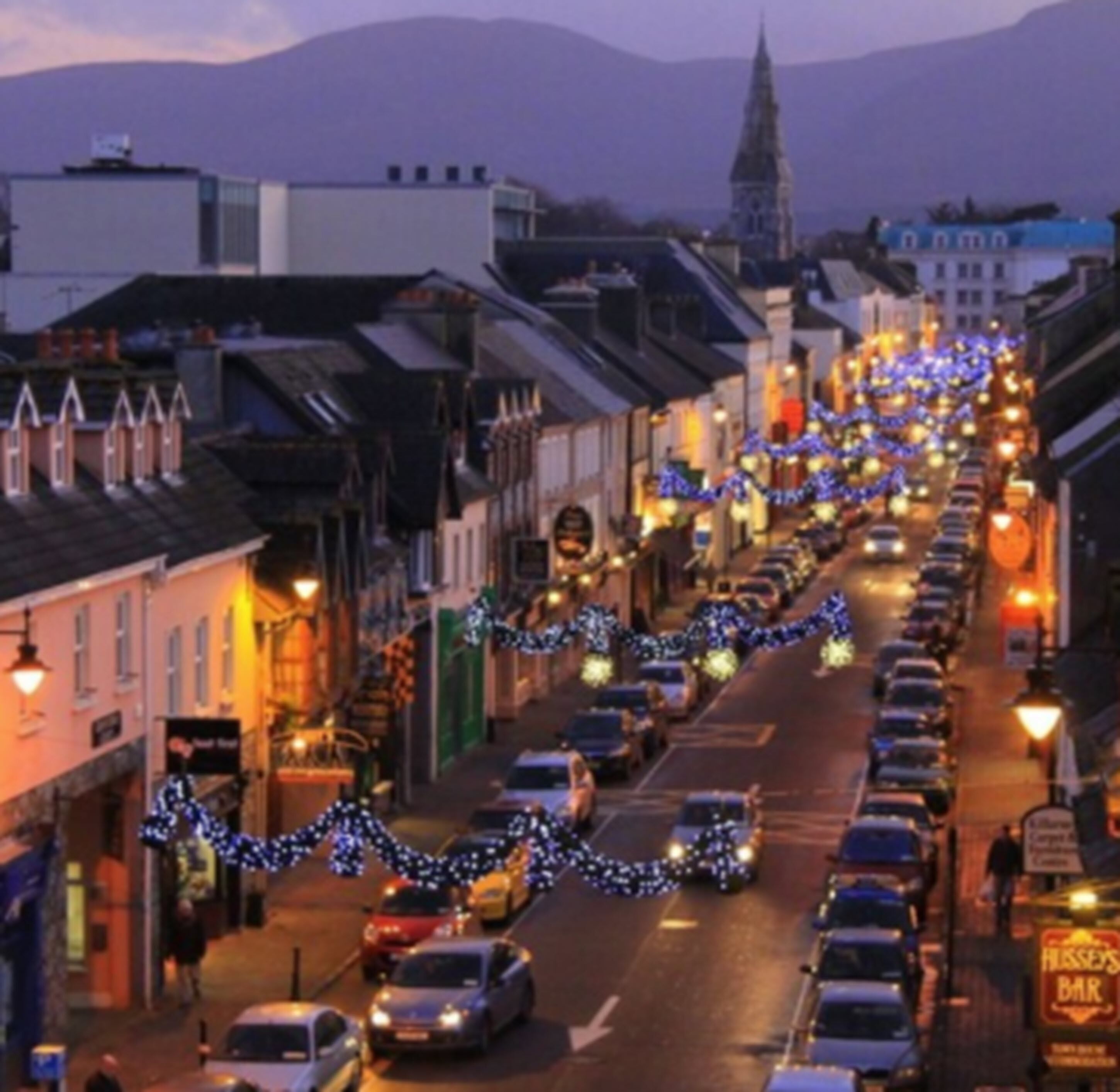 A street lined with buildings, decorated with blue lights, and a clock tower in the background.