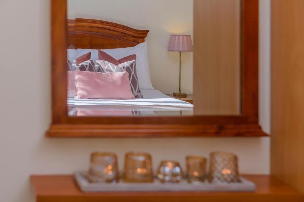 A bedroom with a bed, pillows, a nightstand, a lamp, and a mirror.