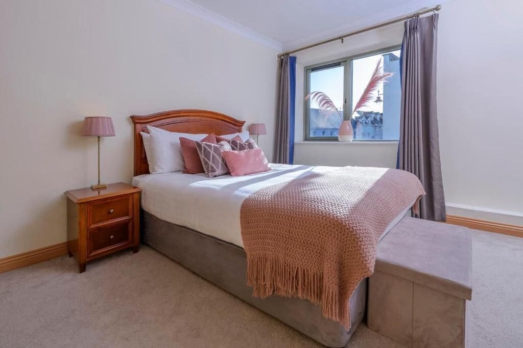 Un dormitorio con cama, mesitas de noche, una ventana con cortinas y vistas al exterior.