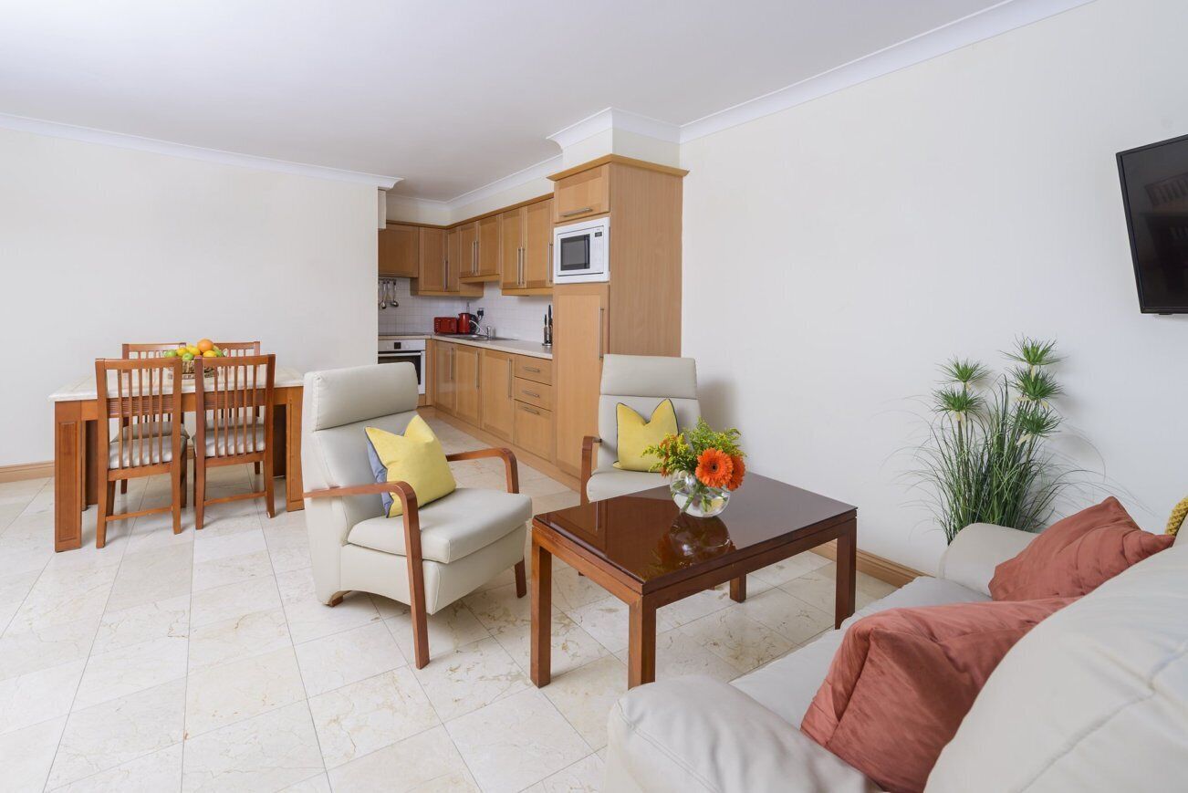 A living room with a sofa, two armchairs, a coffee table, a dining table with chairs, and a kitchen area in the background.