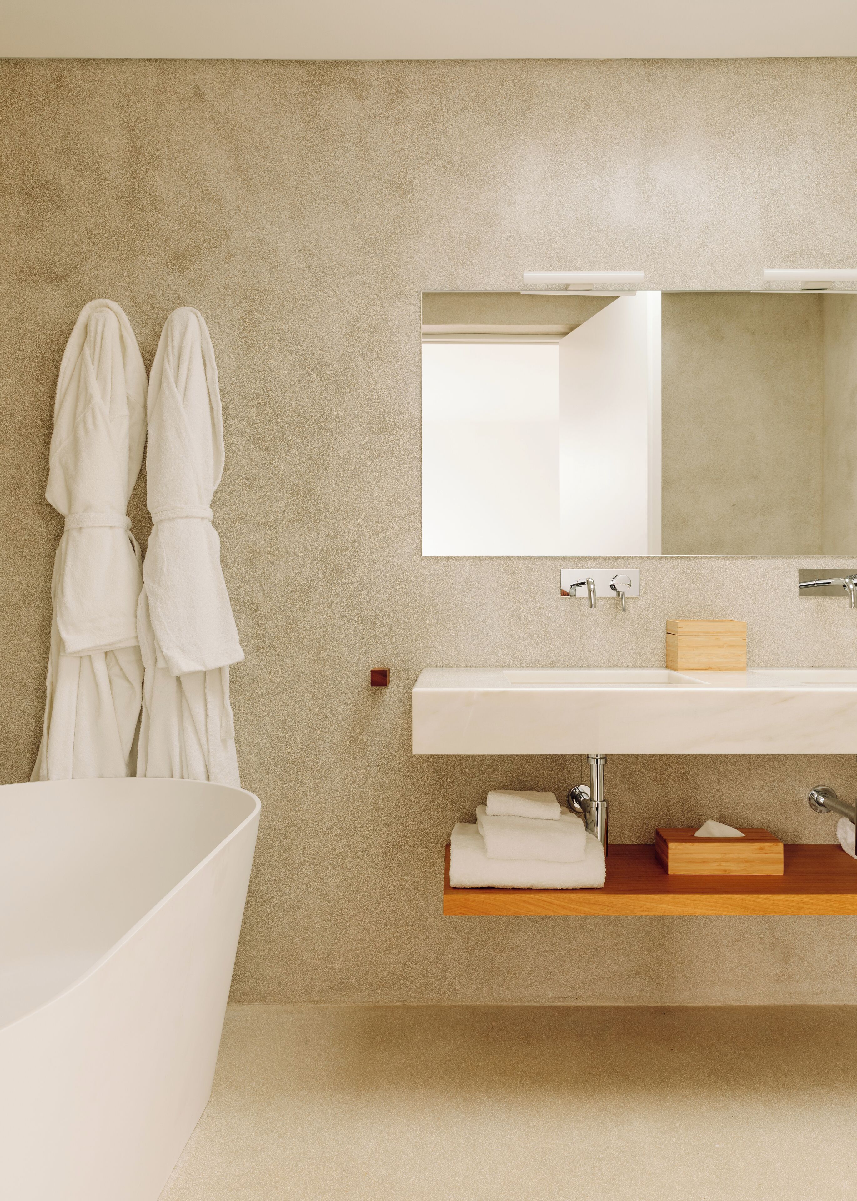 Un baño moderno con una bañera grande, un lavamanos blanco y un espejo encima. Hay dos toallas blancas colgadas en la pared y un caja de madera sobre el lavamanos.
