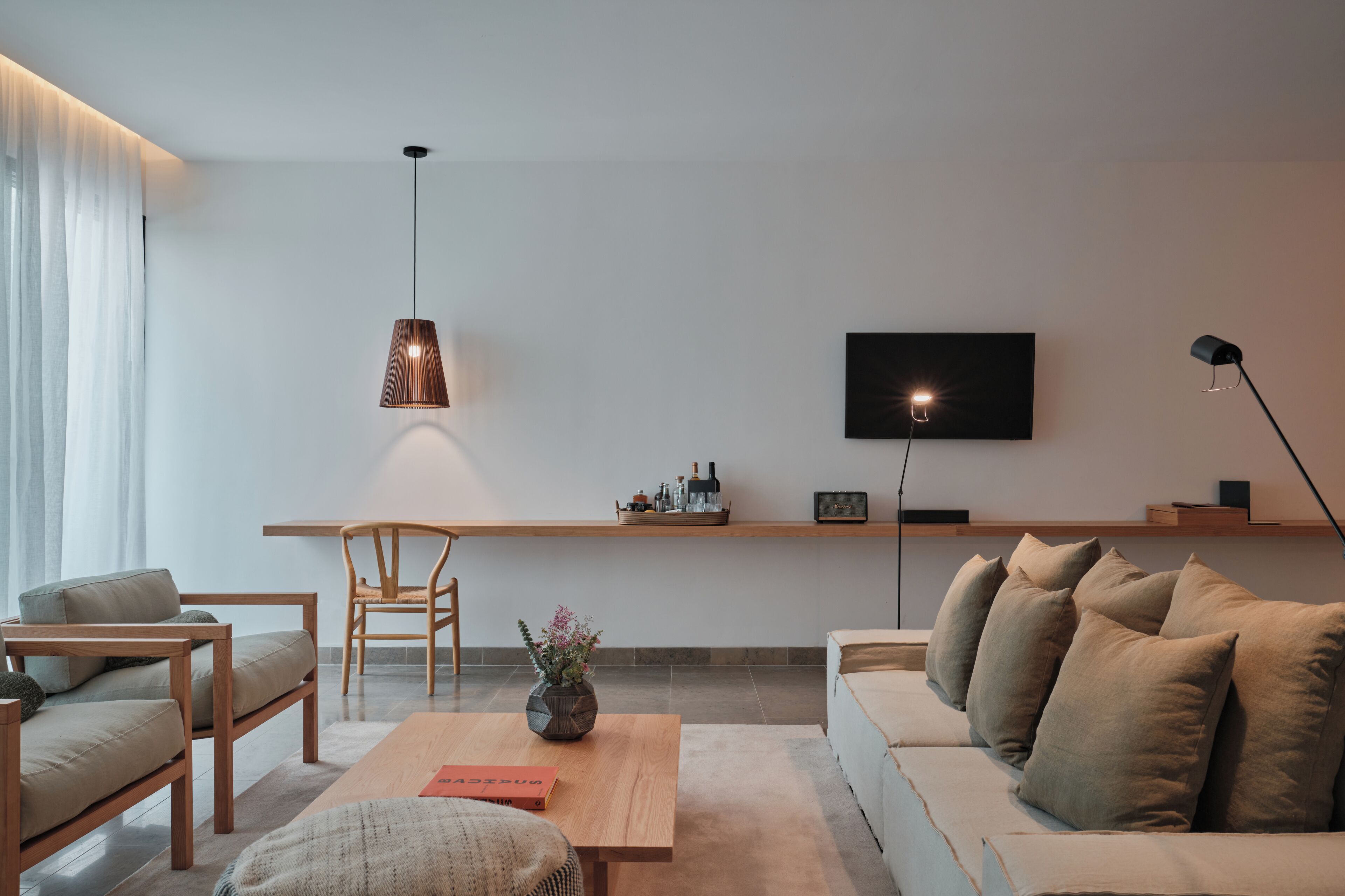 Ein modernes Wohnzimmer mit einer Couch, einem Holztisch, einem Sessel, einem an der Wand befestigten Fernseher und einer Pendelleuchte.