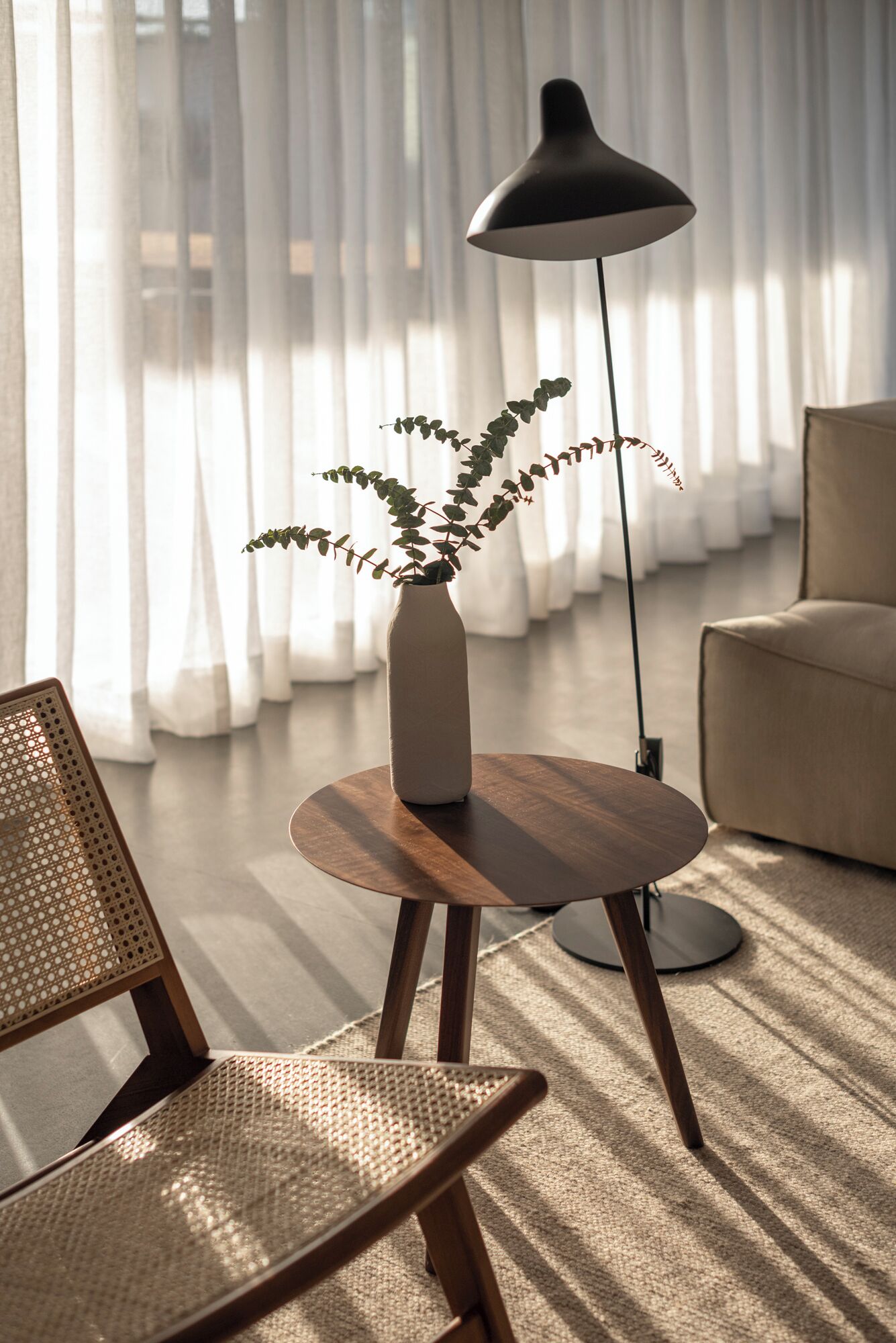 A modern living room with a round wooden table, a tall floor lamp, a potted plant, and a beige sofa.