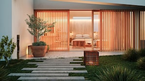Een modern huis met een grote glazen deur die leidt naar een slaapkamer. Er is een houten hek en een bloempot in de voortuin.