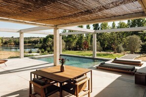 An outdoor patio with a pool, wooden furniture, and a view of the surrounding landscape.