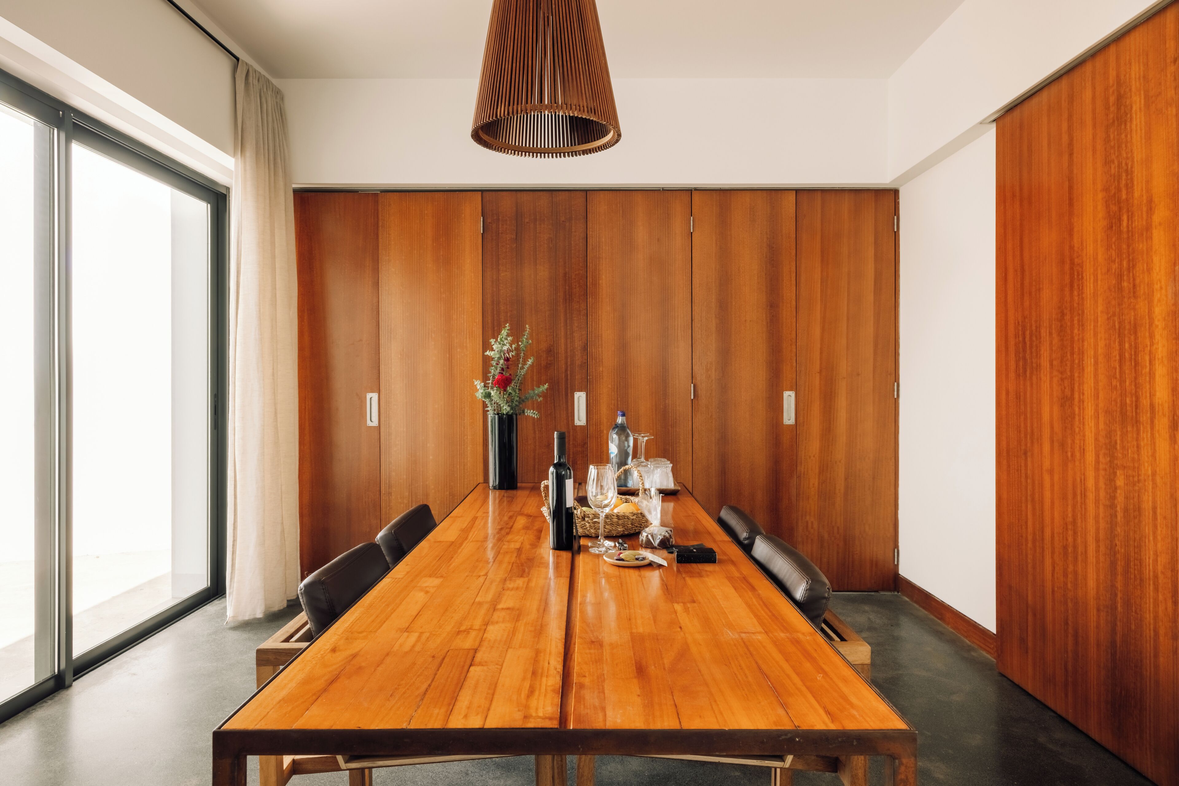 A conference room with a wooden table, chairs, a vase with flowers, a bottle, and glasses.