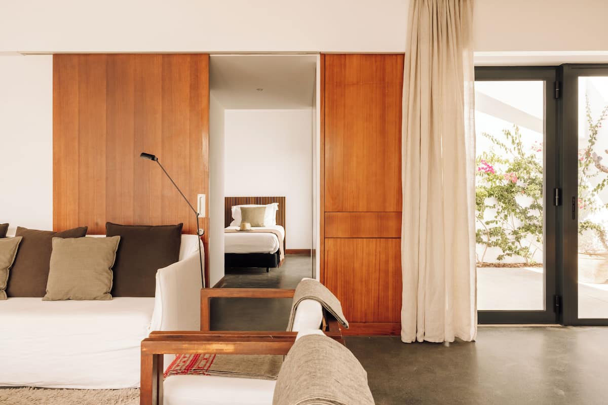 A modern hotel room with a wooden accent wall, a sofa, a bed, and a sliding glass door to the outside.