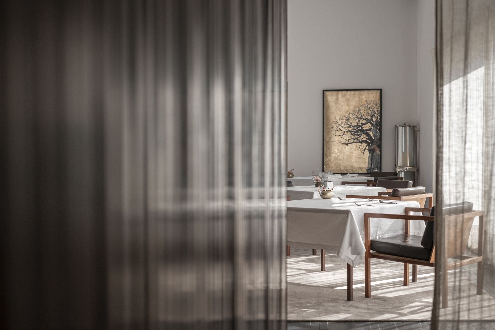 A modern dining area with a large painting, a tall lamp, and a view through a window.