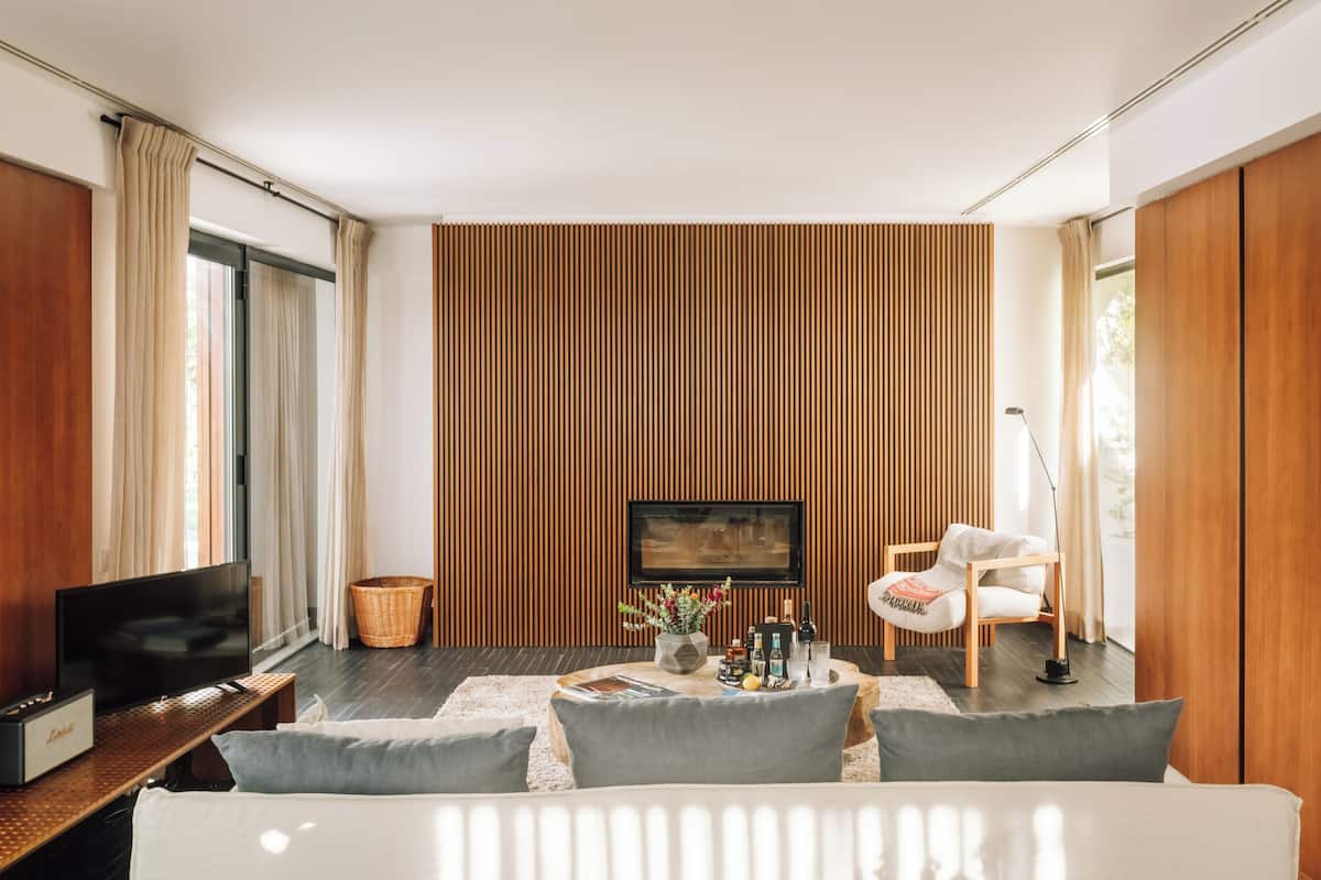 A modern living room with a large flat-screen TV, a sofa, a coffee table with drinks and snacks, and a wooden accent wall.