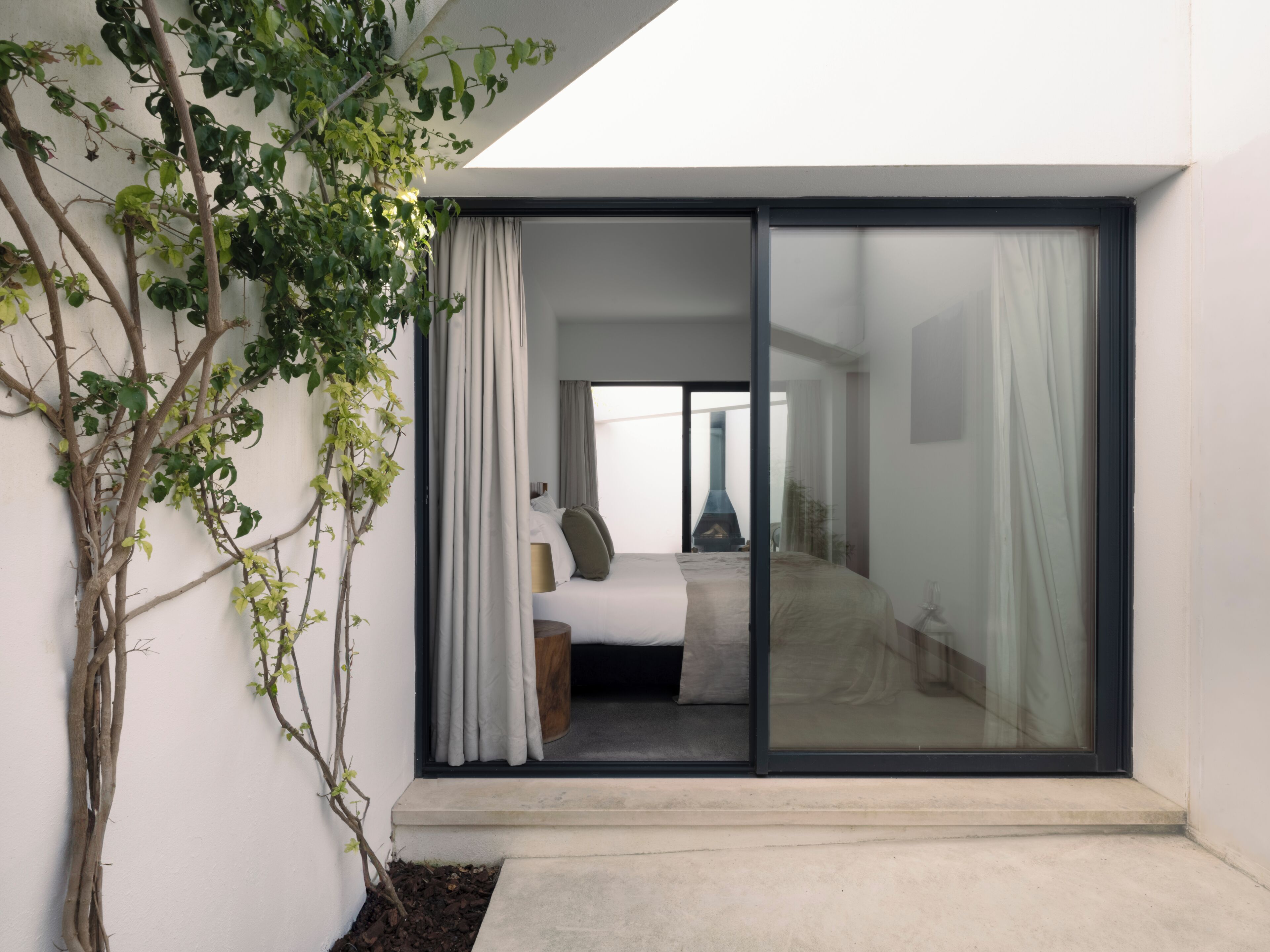 A modern bedroom with a large sliding glass door leading to a balcony, a bed with a headboard, and a visible fireplace in the background.