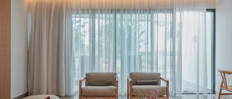 A modern living room with two armchairs, a sofa, and a large window with sheer curtains.