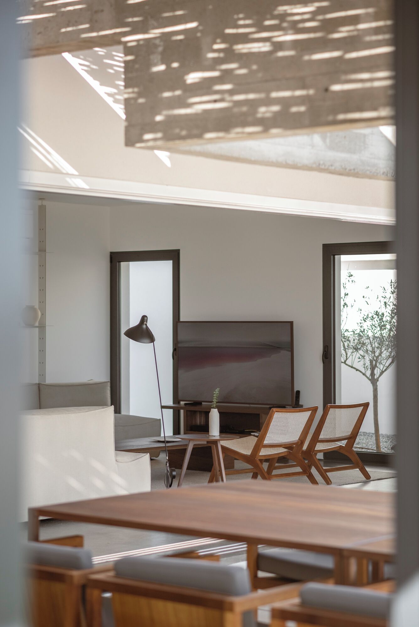 Un salon moderne doté d’un grand téléviseur à écran plat, de meubles en bois et offrant une vue sur un arbre par la fenêtre.