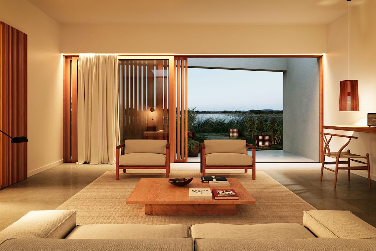 A modern living room with a large sliding glass door leading to a balcony, two armchairs, a coffee table, and a small desk area.