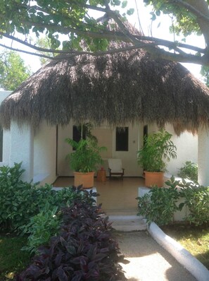 A thatched-roof structure with a white exterior, two potted plants, and a chair in the center.