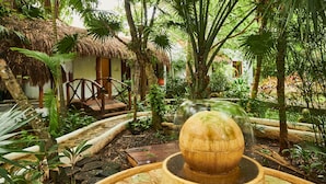 A lush garden with a thatched-roof hut, a wooden bridge, and a water feature. - Amarte Maroma Hotel Eco Boutique Spa (Playa del Carmen)