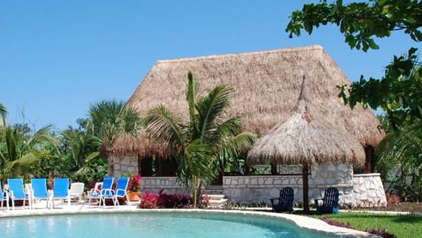 A pool with blue water, surrounded by lounge chairs and a thatched-roof building. - Amarte Maroma Hotel Eco Boutique Spa (Playa del Carmen)