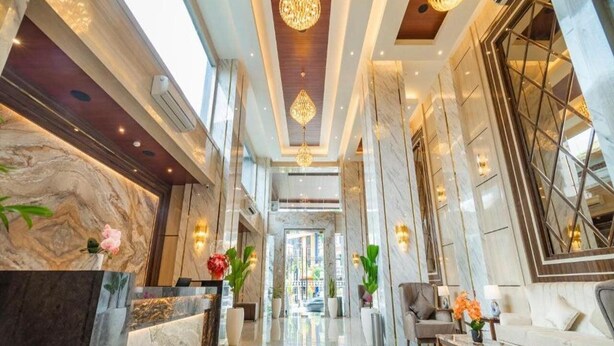 En hotellobby med väggar i marmor, en receptionsdisk, en sittgrupp och dekorativ belysning.