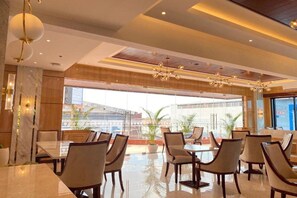 A modern dining area with tables and chairs, large windows, and a view of the city. - POP! Hotel Teuku Umar Denpasar - Bali (Denpasar)