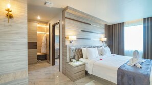 Une chambre d’hôtel avec un grand lit, des tables de chevet, une robe suspendue, un miroir et une fenêtre avec des rideaux.