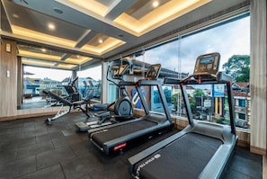 Ein Fitnessraum mit Laufbändern, Rudergerät und Ergometer, mit Blick auf Gebäude durch große Fenster.
