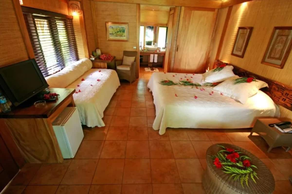 A hotel room with two beds, a small desk with a television, a chair, and a small table.