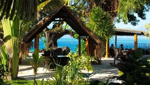 Un restaurante frente al mar con terraza, techo de paja y vistas al océano.