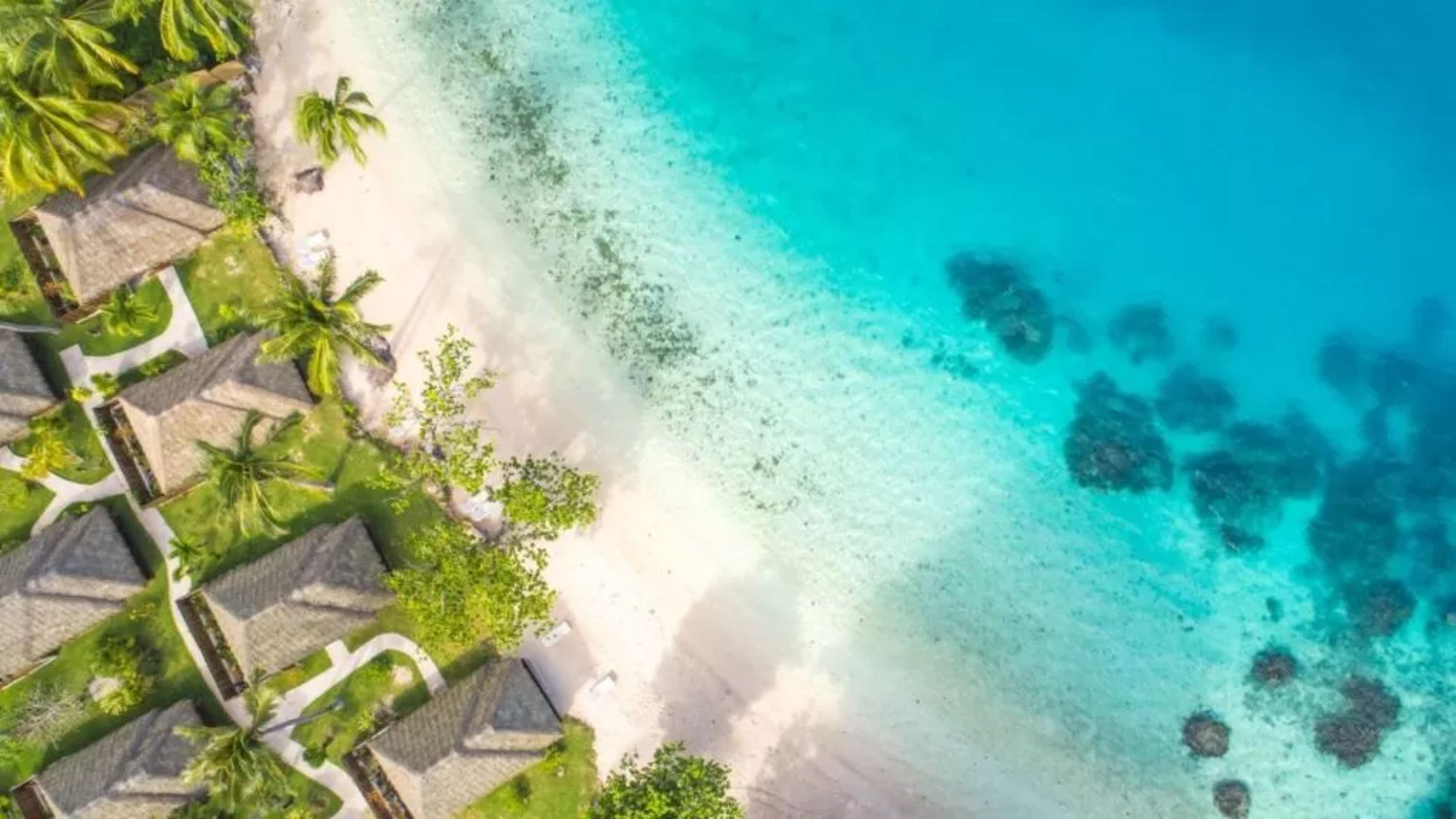Un resort con bungalós sobre el agua, una playa de arena y aguas turquesas cristalinas.