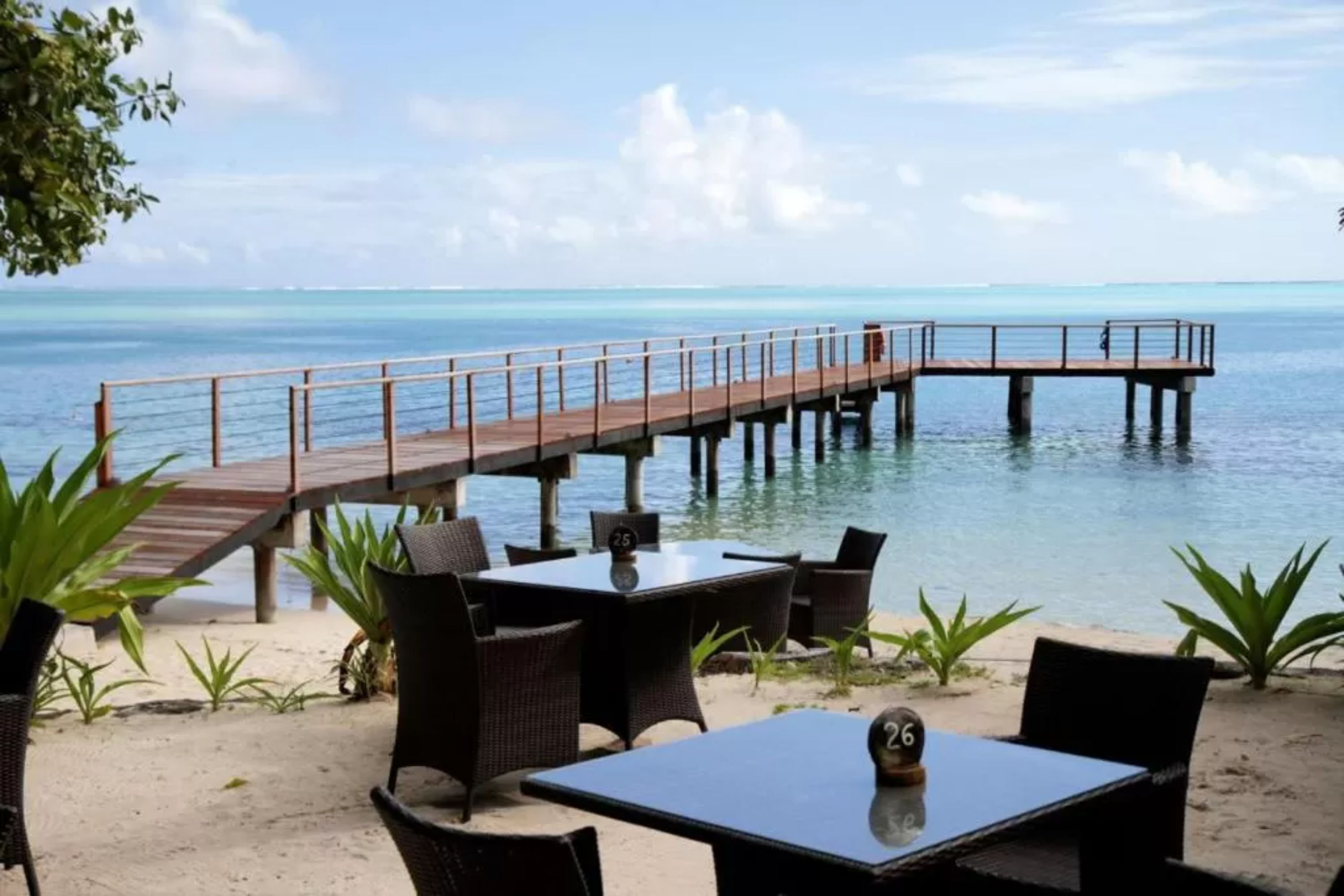A beachside restaurant with outdoor seating, a wooden deck, and a view of the ocean.